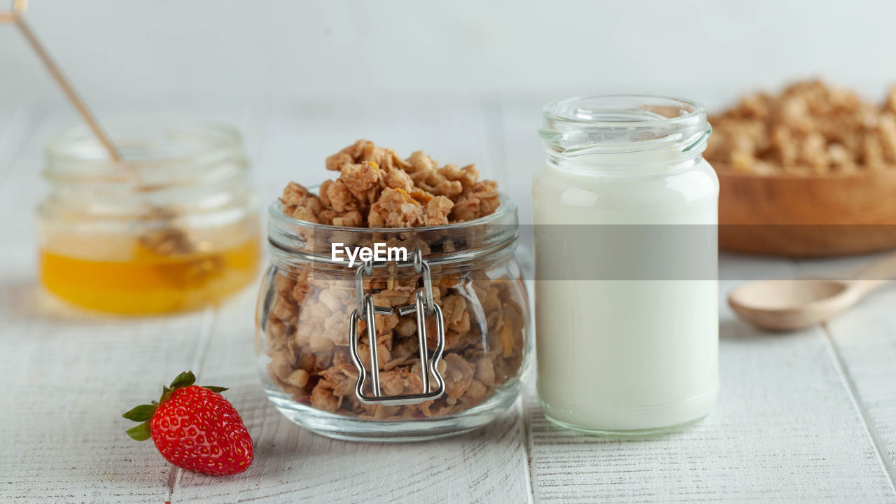 Banner with homemade granola, milk in a jar, honey and strawberries on a wooden background. 
