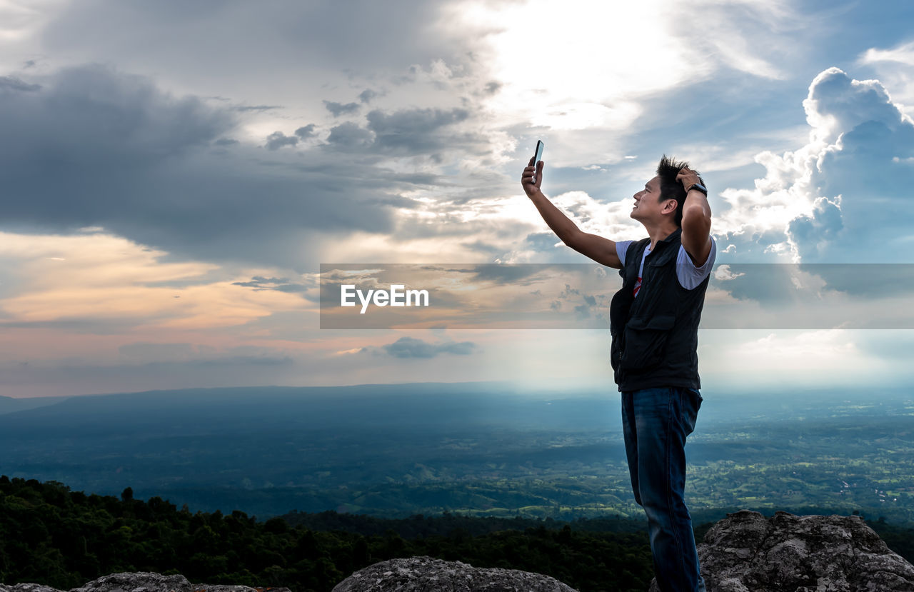 FULL LENGTH OF MAN STANDING ON ROCKS AT MOUNTAIN AGAINST SKY