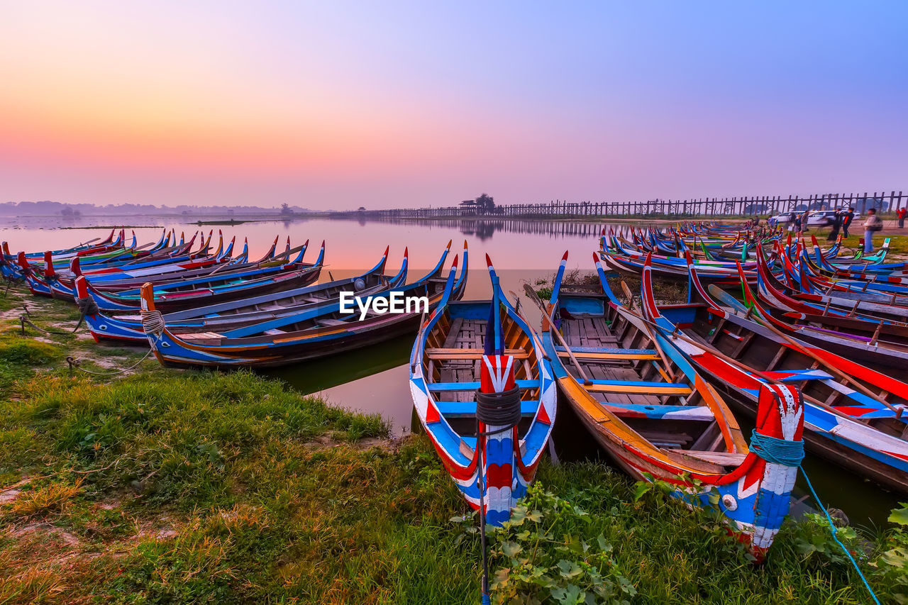 Fishing boats moored at riverbank against sky during sunset