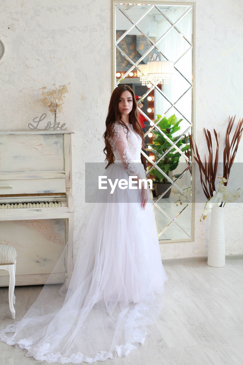 Portrait of young bride standing against wall at home