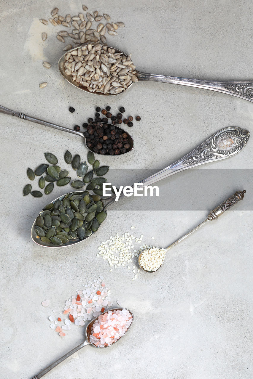 Collection of spices and seeds on a spoons on gray background.