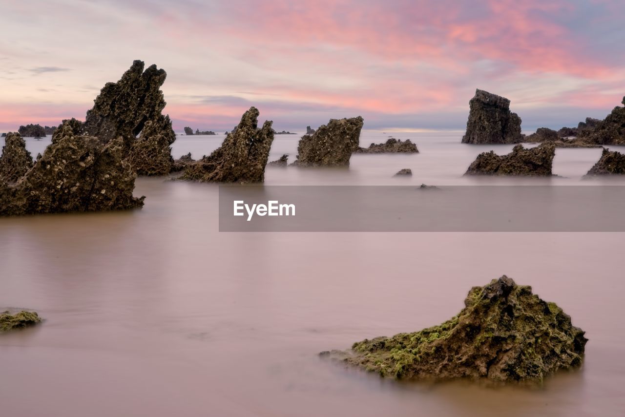 Rocks appear in the silky water of a beach in spain