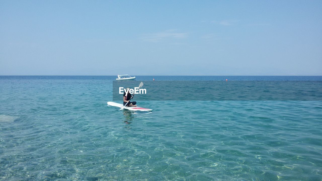 Woman paddleboarding on sea against clear sky