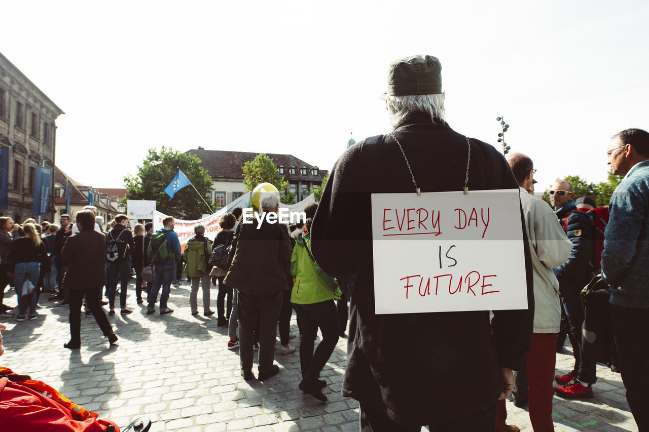 REAR VIEW OF PEOPLE WALKING ON STREET IN CITY AGAINST SKY