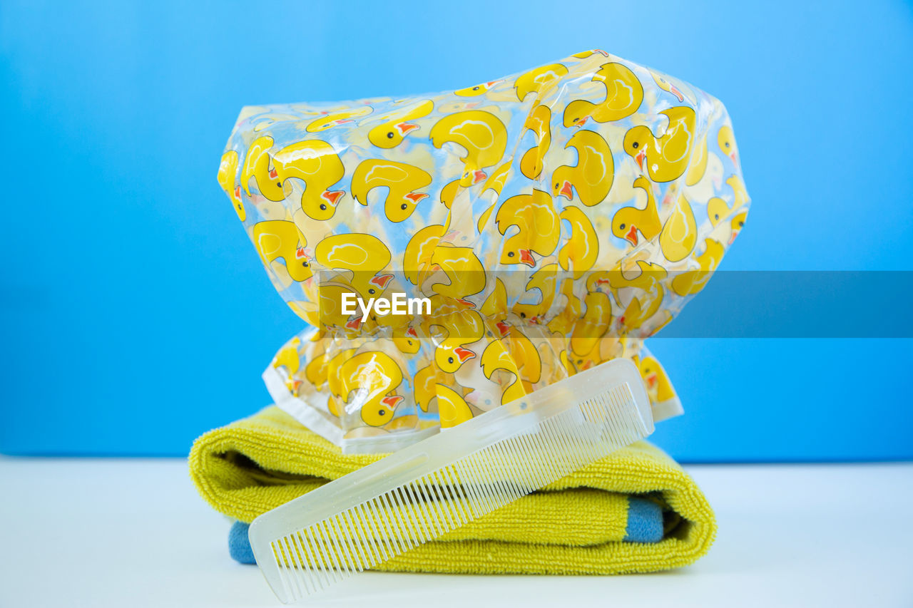 Close-up of plastic hat with towel and hairbrush table against blue background