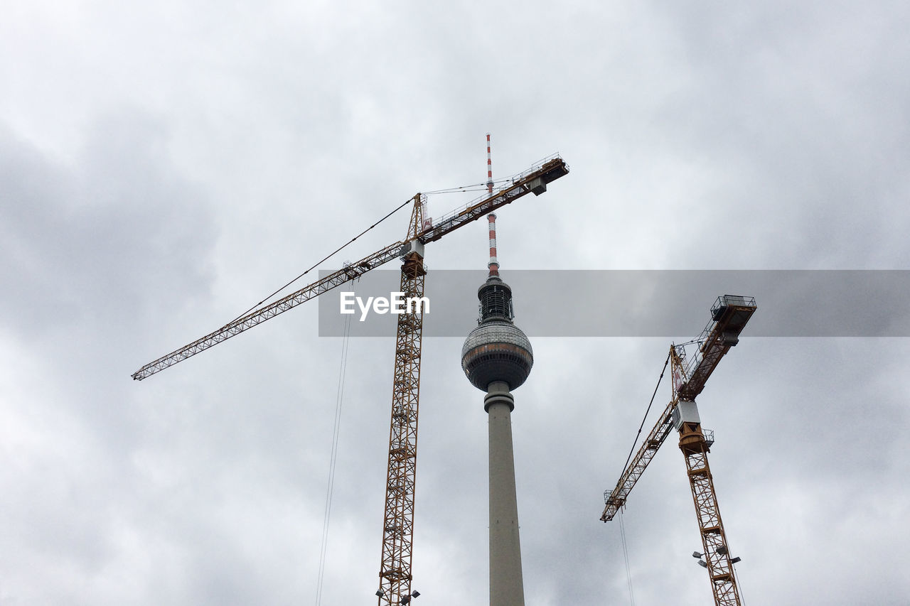 Low angle view of fernsehturm and cranes against sky