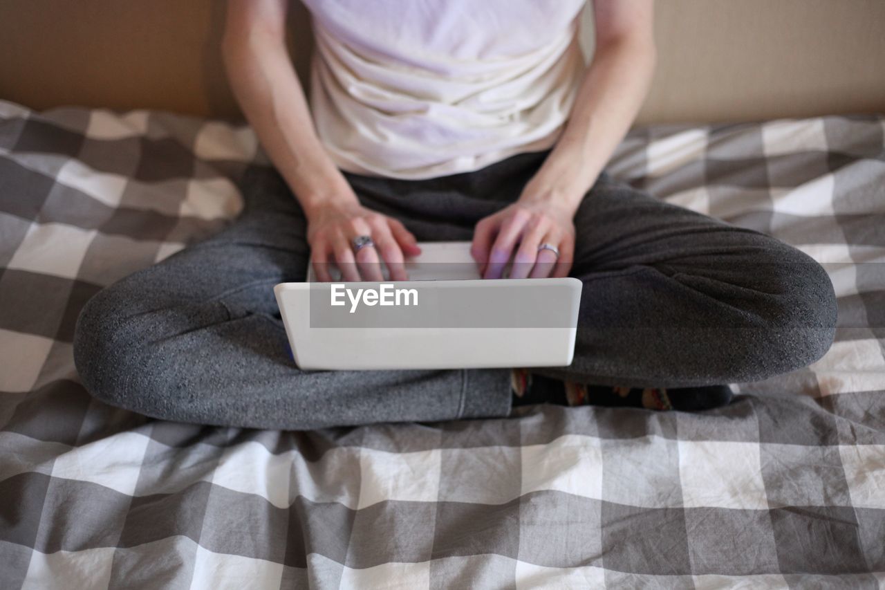 MIDSECTION OF MAN USING SMART PHONE WHILE SITTING ON BED