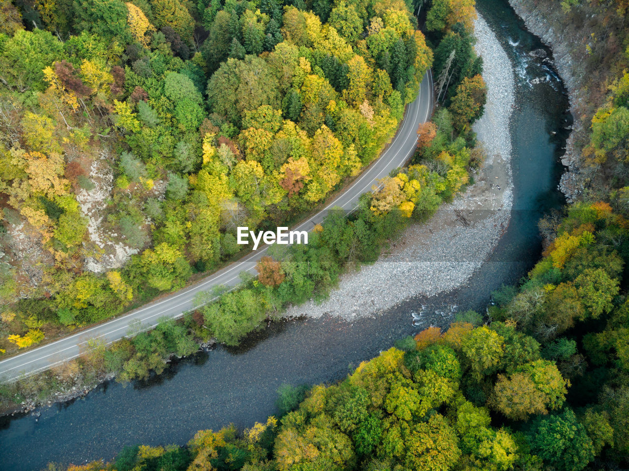 Aerial view of the road and colorful autumn forest with a mountain river in russia, adygea