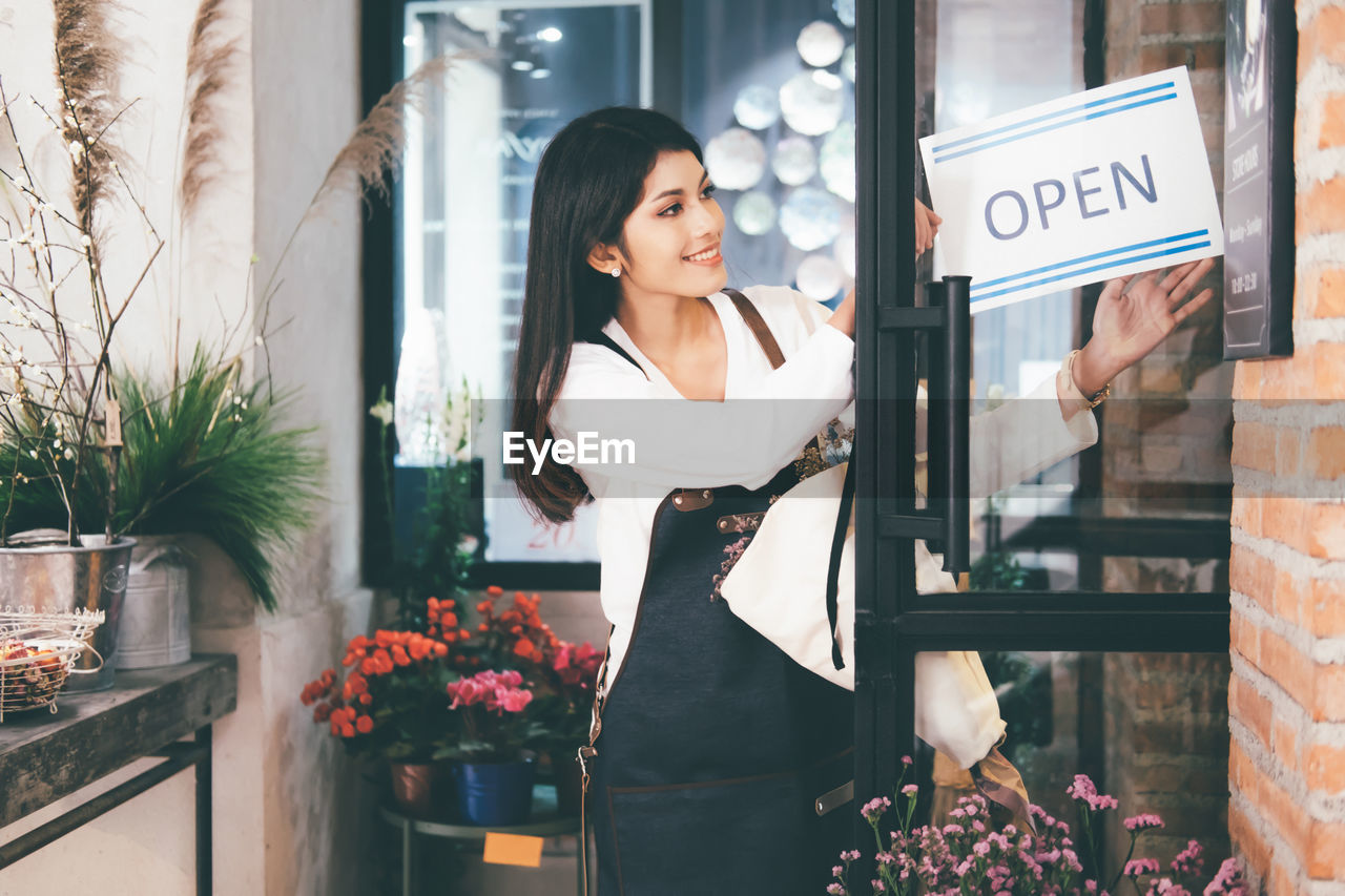 Female owner standing with open sign standing at doorway