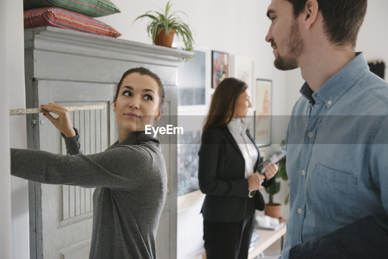 Man looking at woman holding tape measure with female realtor in background