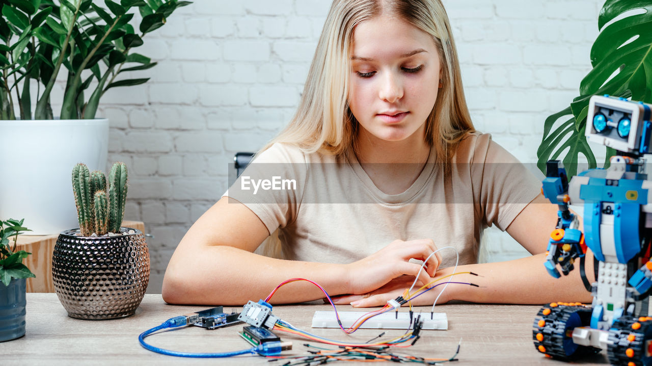 A blonde teen girl plugging cables to sensor chips while learning arduino coding and robotics