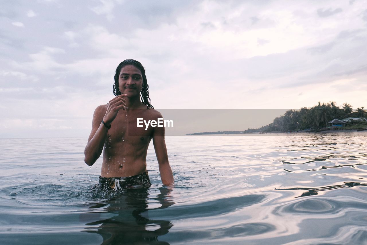 Portrait of shirtless man standing in sea against sky