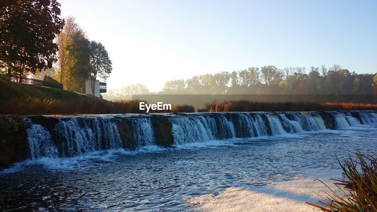 SCENIC VIEW OF WATERFALL BY TREES AGAINST SKY