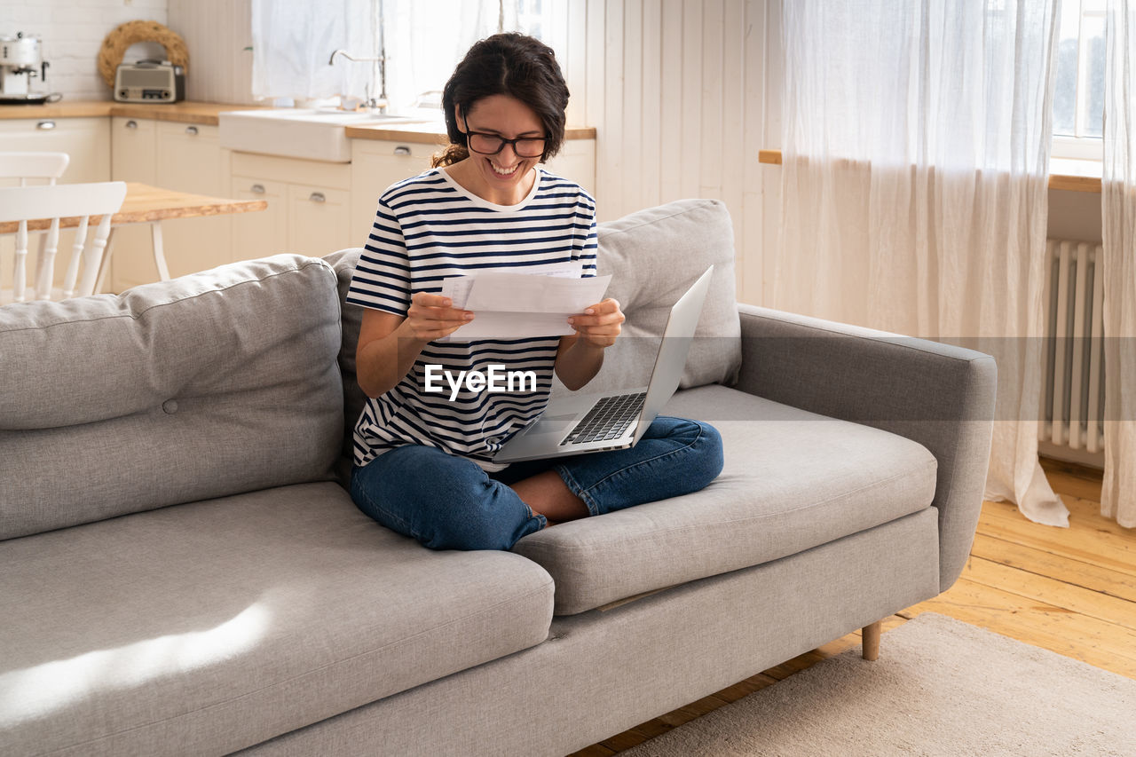 Full length of young woman sitting on sofa at home