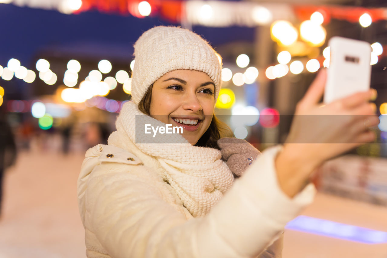 PORTRAIT OF SMILING YOUNG WOMAN STANDING IN CITY