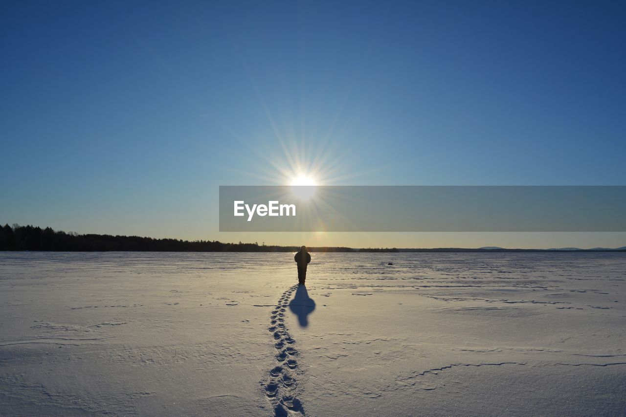 Silhouette person walking on snowcapped landscape against clear blue sky