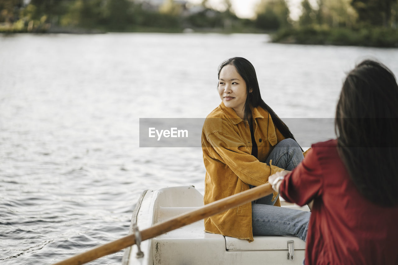 Woman looking away while female friend rowing boat on lake