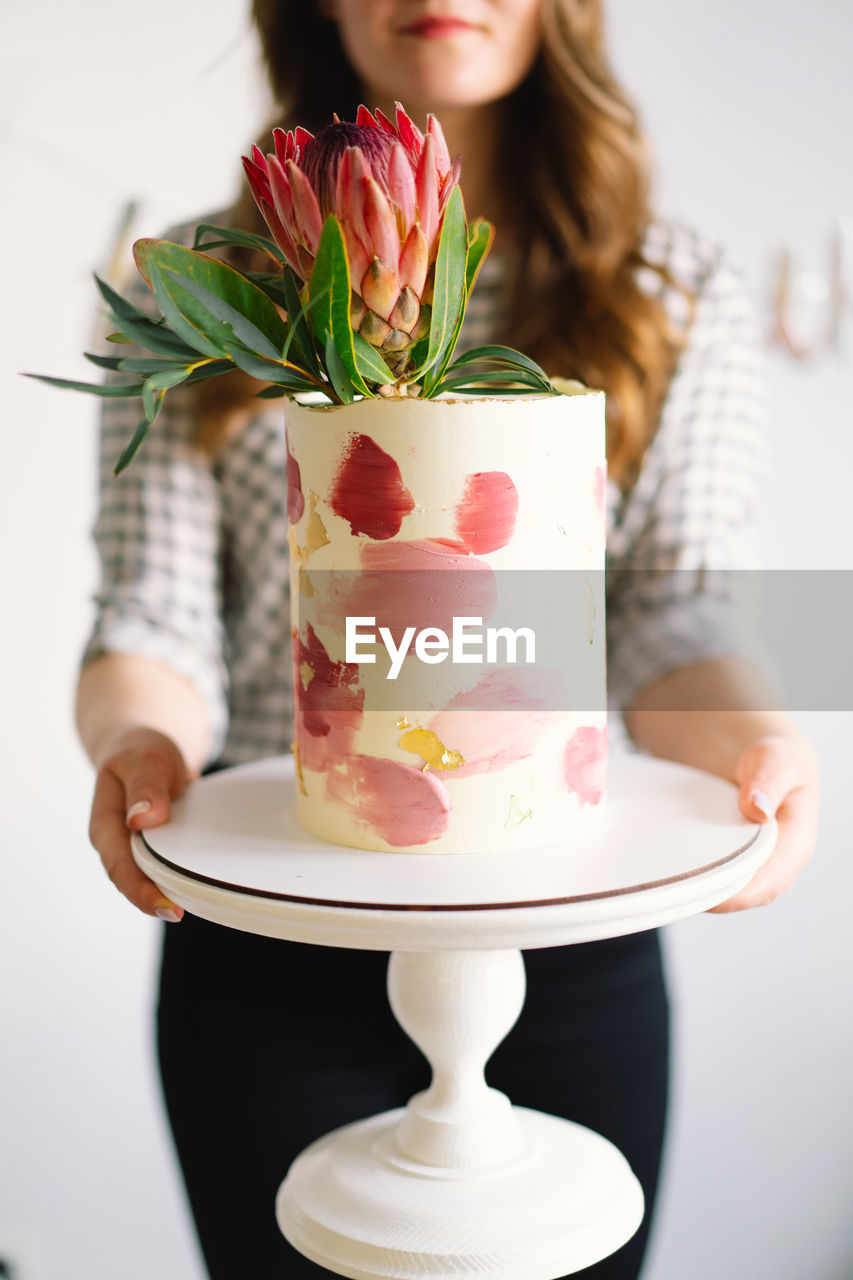 Young woman with birthday cake, close up. the cake is decorated with protea flowers.