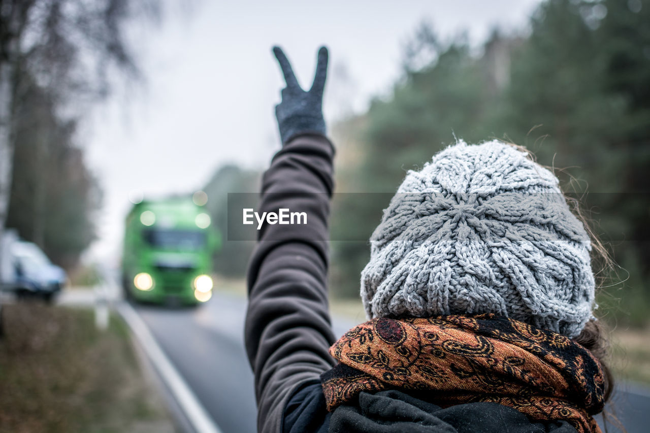 Rear view of woman wearing warm clothing while gesturing peace sign to bus on road