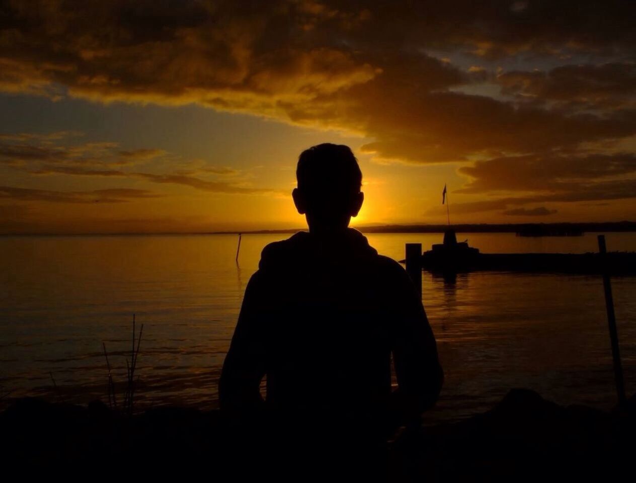 Silhouette rear view of boy standing at beach during sunset