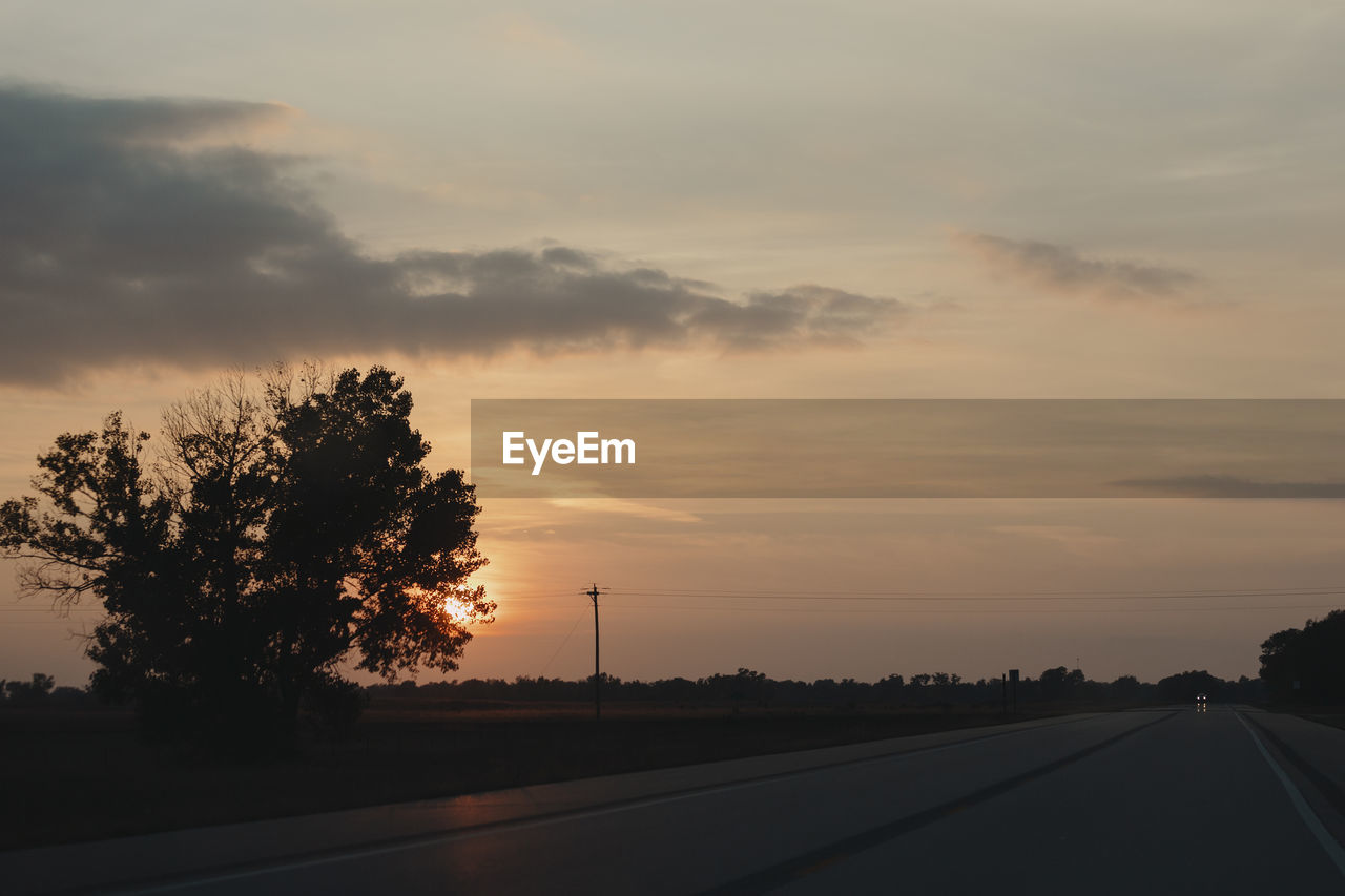 Silhouette trees by road against sky during sunset