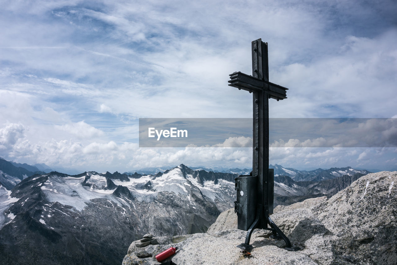 Cross on rock by snowcapped mountains against sky