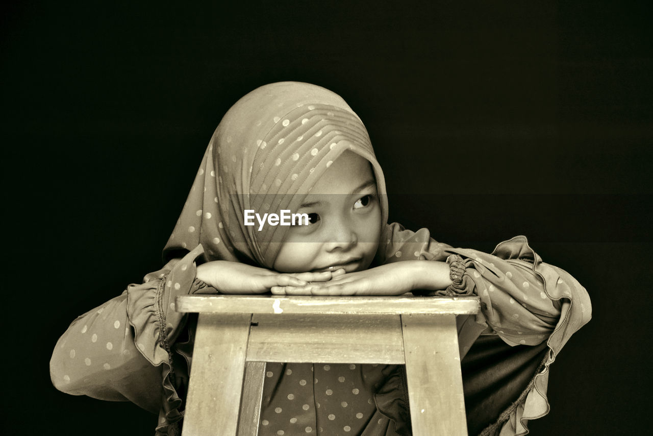 Cute girl wearing hijab looking away against black background