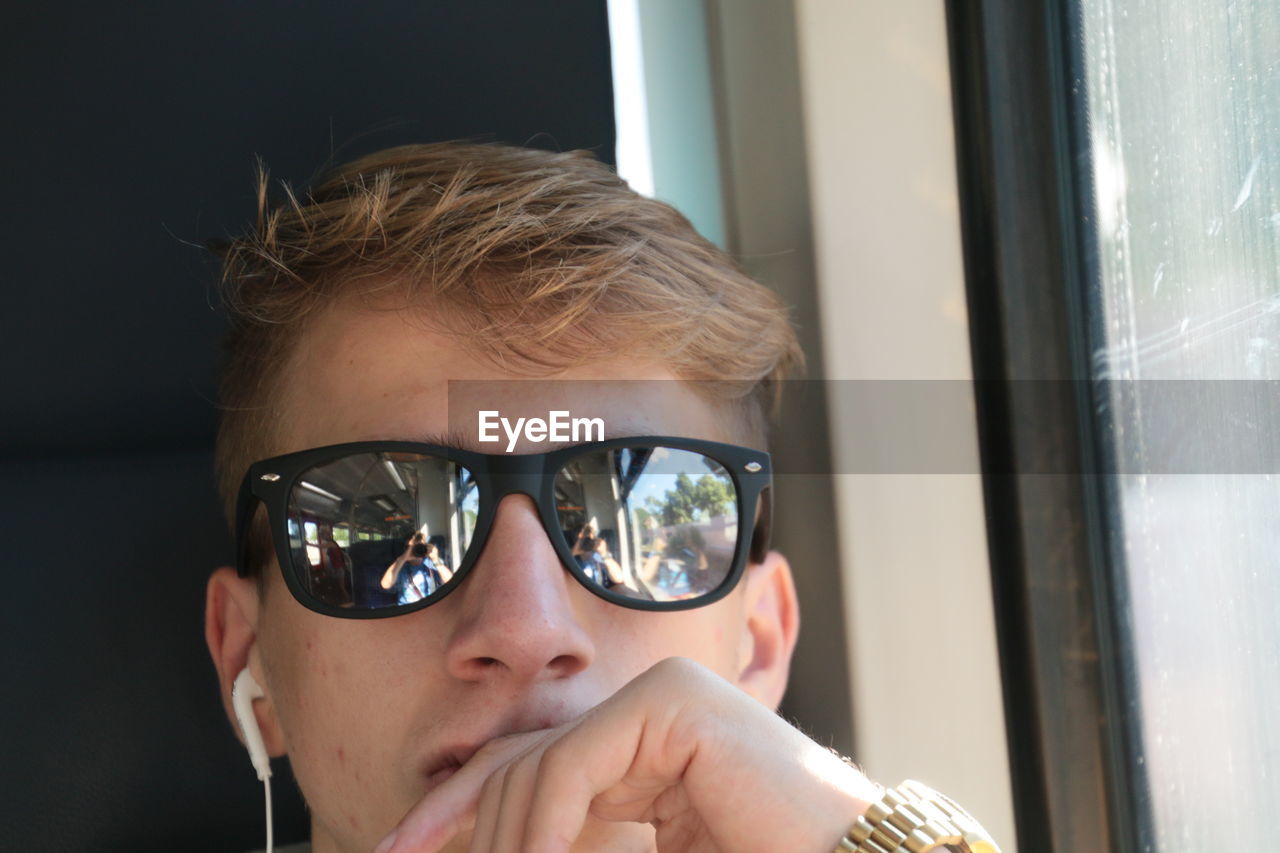 Close-up of man wearing sunglasses with reflection of friend photographing while traveling in train