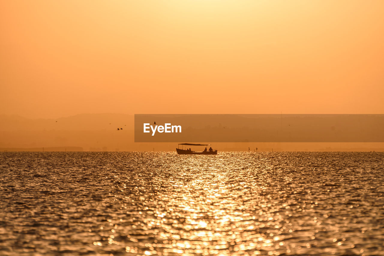 Silhouette boat in sea against orange sky