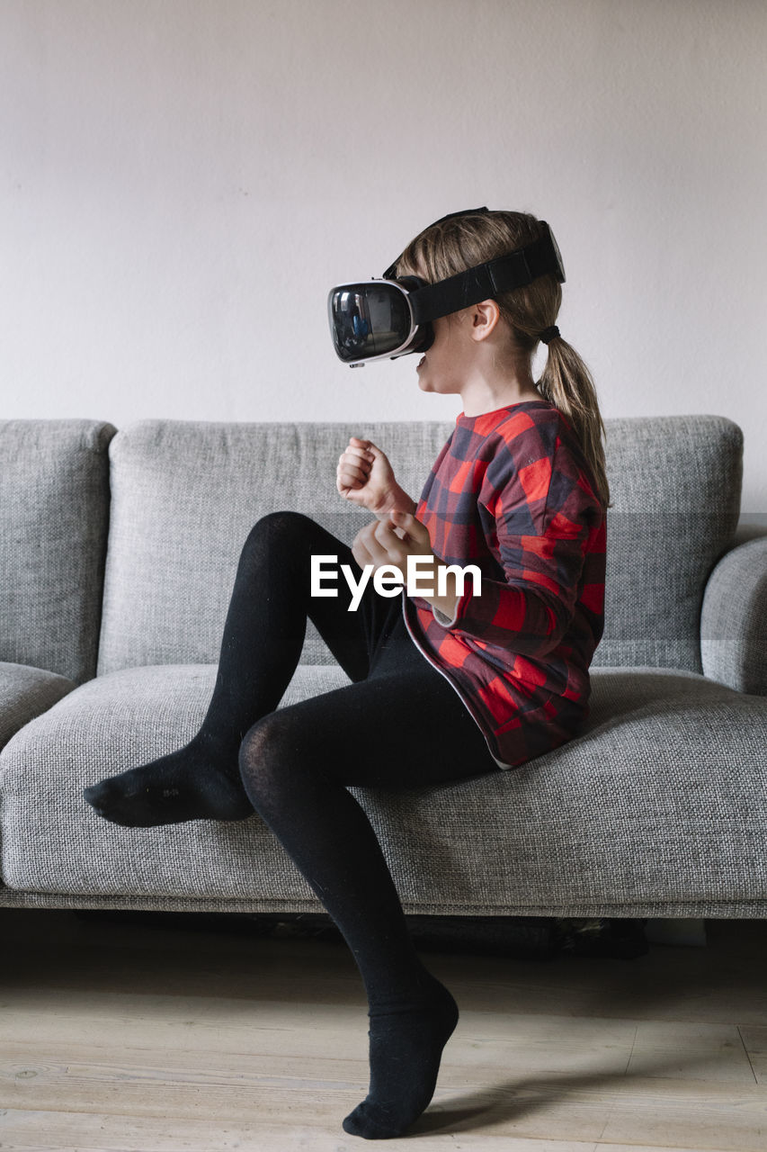 Girl sitting on the couch in the living room using virtual reality glasses