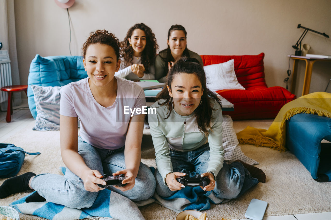 Happy female friends playing video game in living room at home