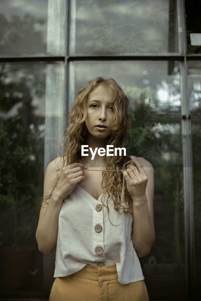 PORTRAIT OF WOMAN STANDING AGAINST WINDOW