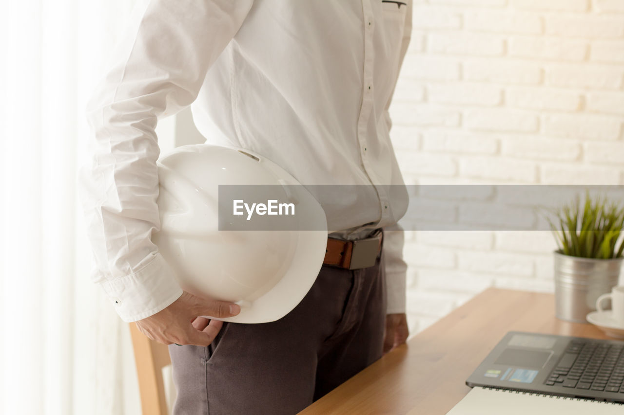 Midsection of engineer standing with hardhat at office