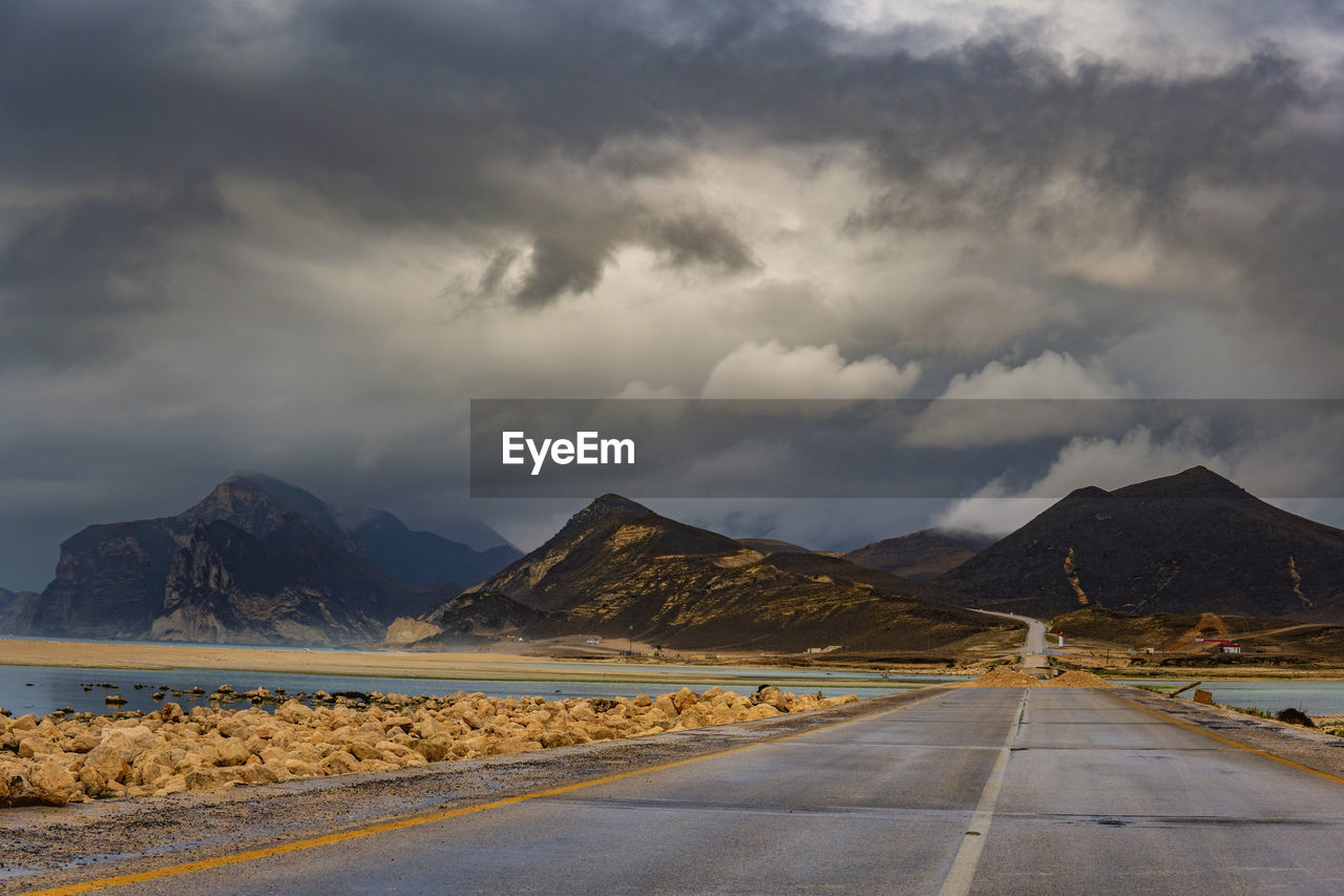 SURFACE LEVEL OF ROAD AGAINST MOUNTAINS AND CLOUDS