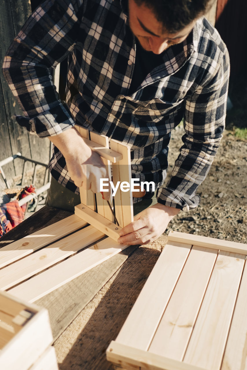 Mid adult male farmer making wooden crate using screwdriver