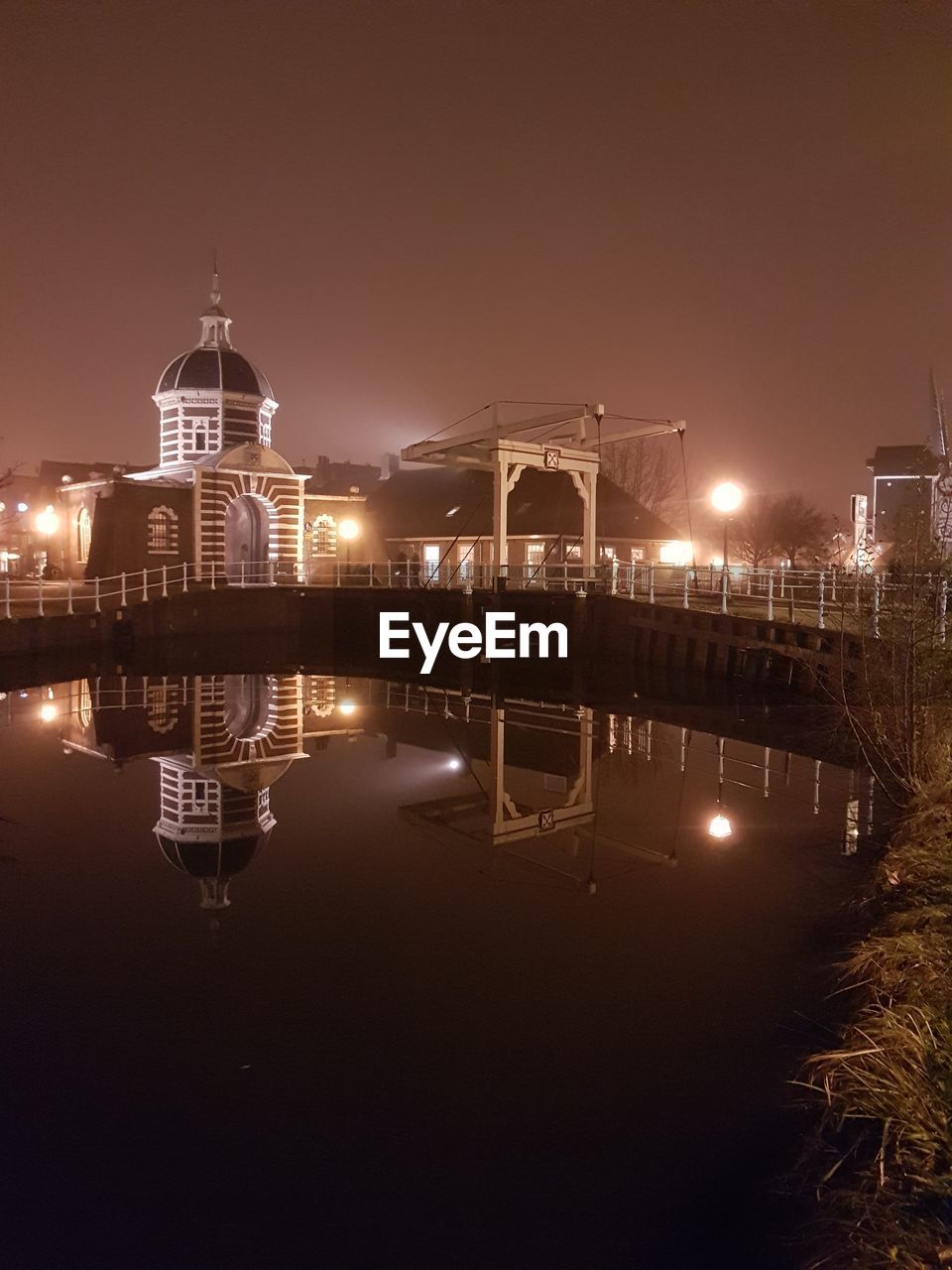 Symmetry view of illuminated bridge by river in city against sky at night