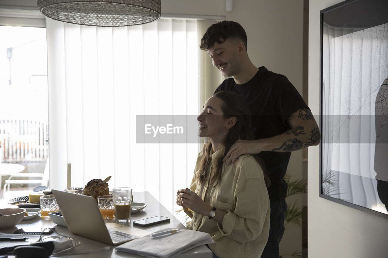 Young man massaging shoulders of girlfriend working at home