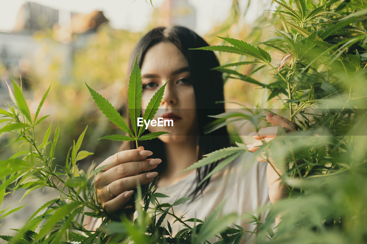 Portrait of young woman holding leaf of cannabis plant