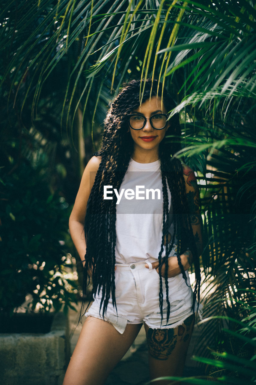 Portrait of young woman standing by trees