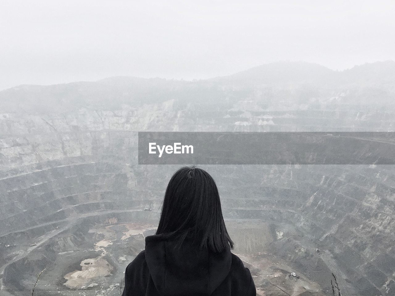 Rear view of woman standing against open-pit mine during foggy weather