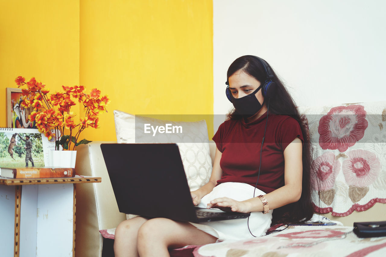 Close up of a young indian girl working on her laptop wearing headphones, work from home concept.