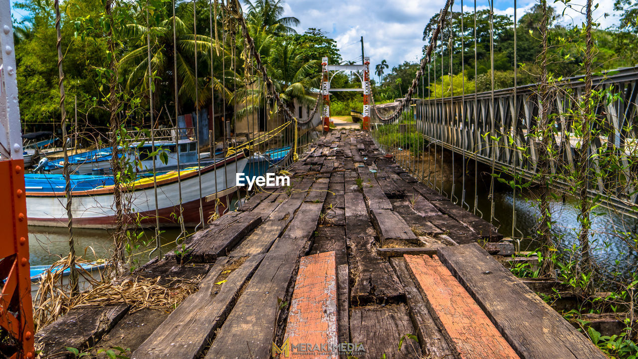 FOOTBRIDGE AMIDST TREES AGAINST SKY