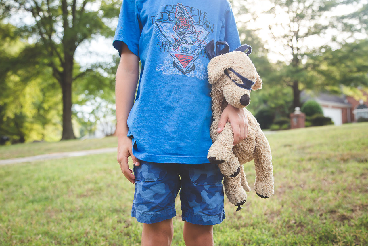 Midsection of boy holding stuffed toy on grassy field