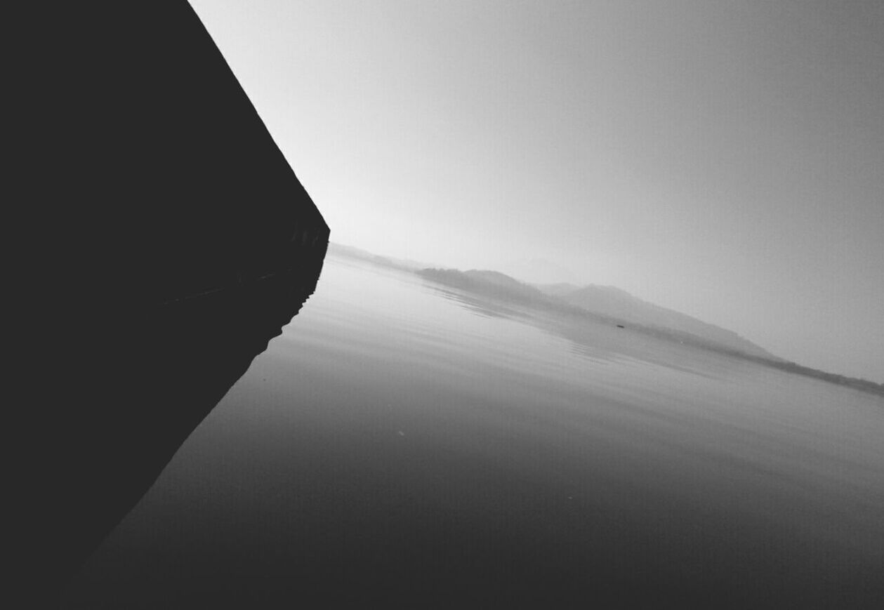 Tilt image of silhouette wall by river against clear sky at dusk