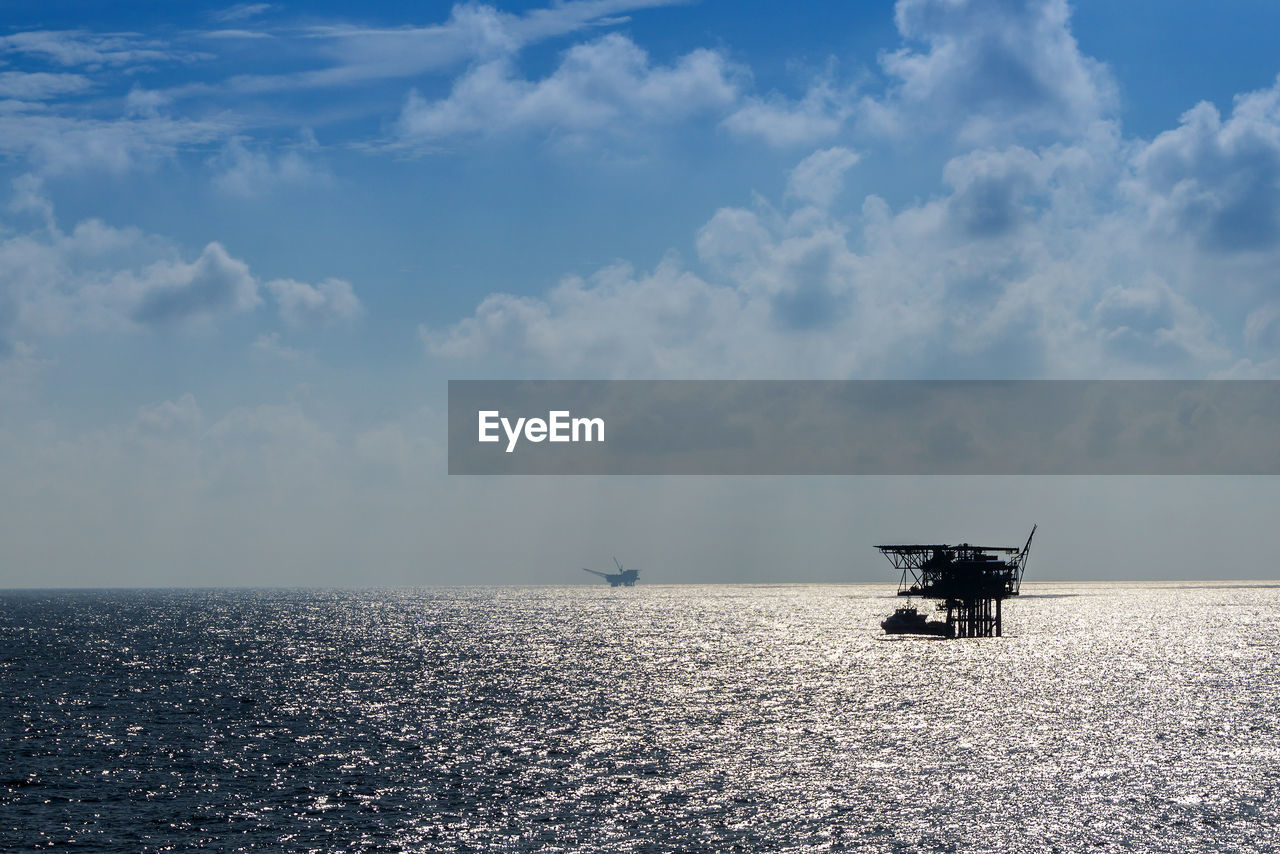 Silhouette oil drill amidst sea against sky