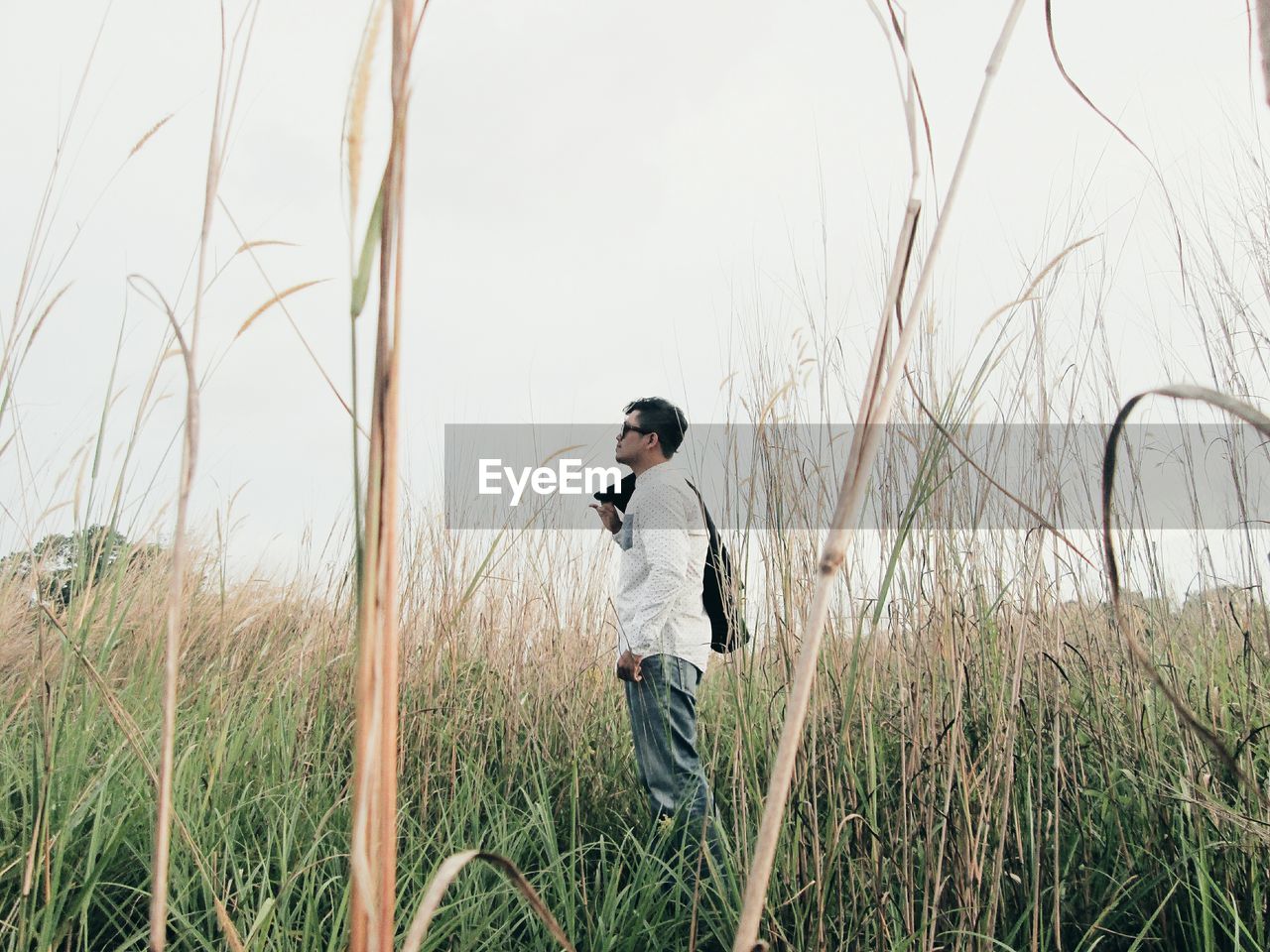 Side view of man standing on field against sky