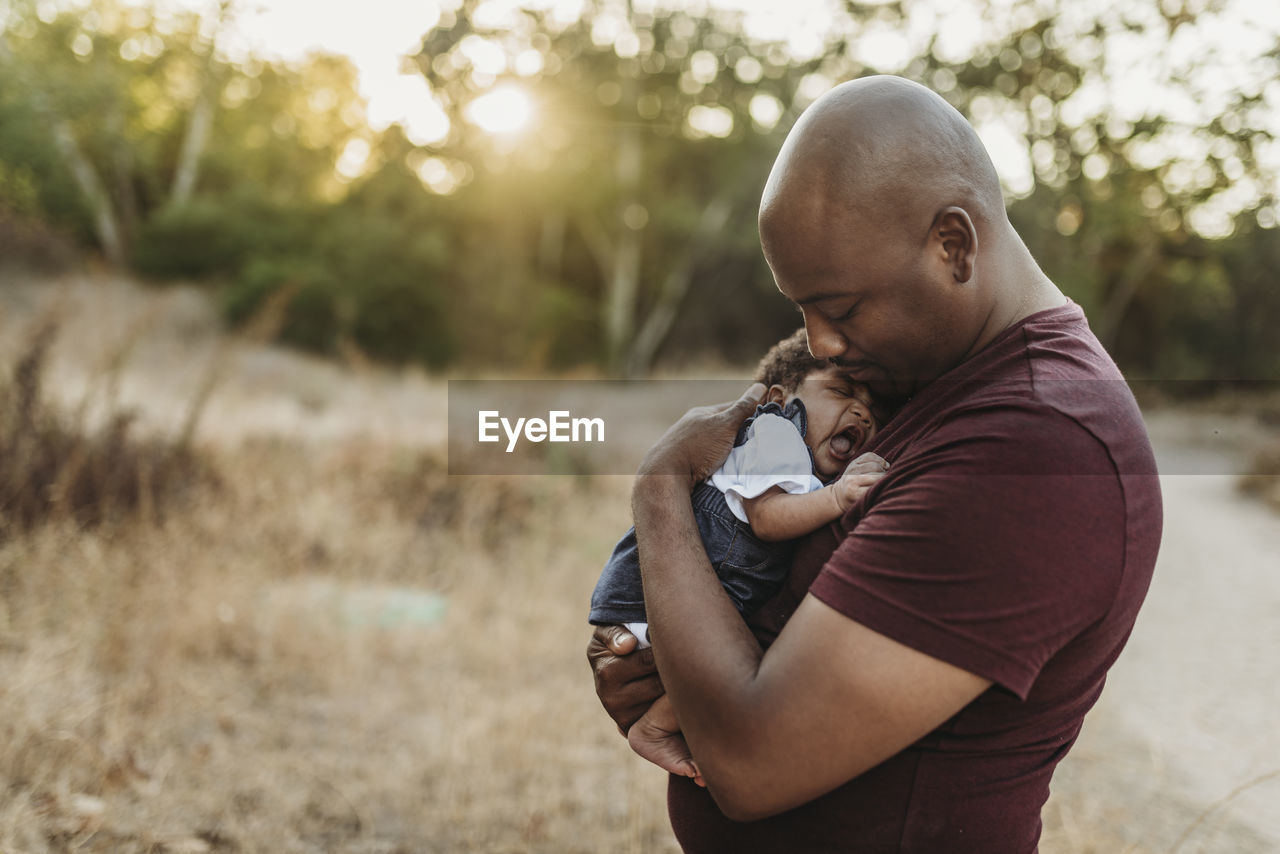 Close up of sweet father cuddling newborn girl in backlit field