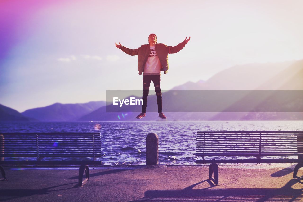 FULL LENGTH OF MAN JUMPING ON LANDSCAPE AGAINST SKY