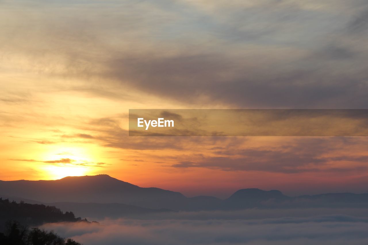 Scenic view of cloud covered landscape and mountains at sunset