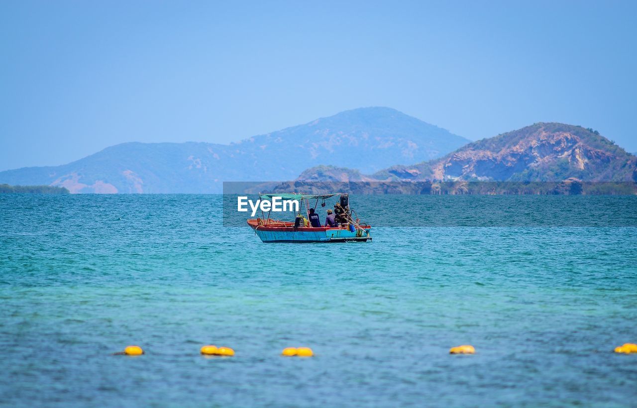 People in boat sailing on sea against clear sky